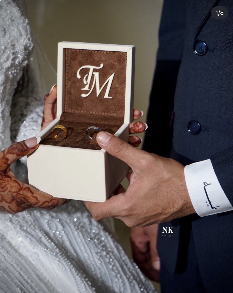 Groom opening a monogrammed ring box beside the bride’s henna-painted hands