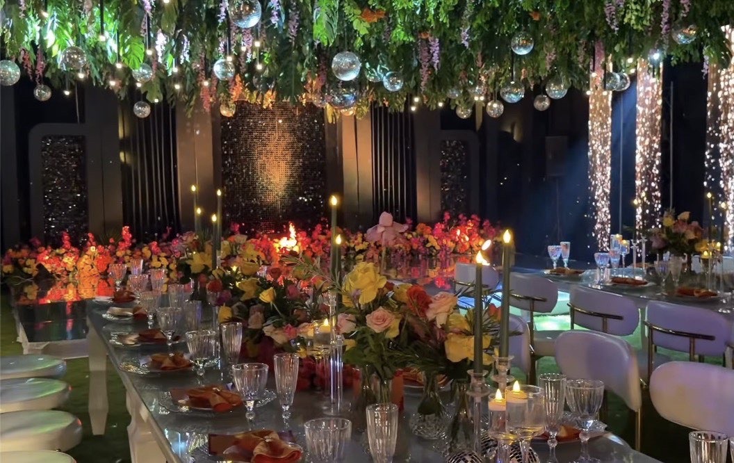 Reception tablescape under a canopy of greenery with candles and red and orange florals