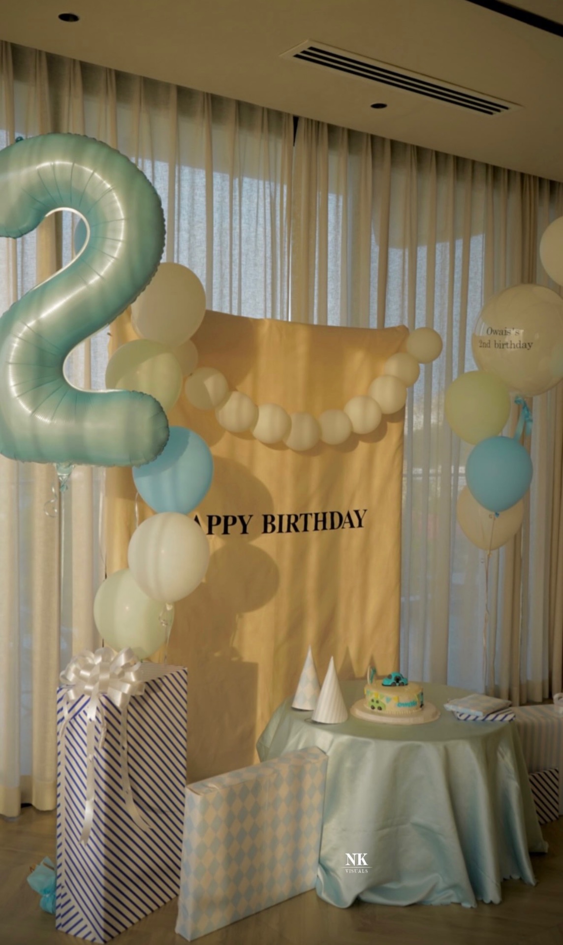 Pastel blue second-birthday backdrop with balloons, gifts and cake